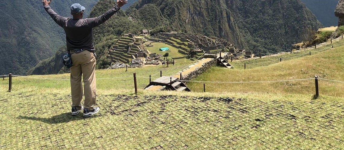 Person enjoying panoramic view of Machu Picchu and surrounding mountains.