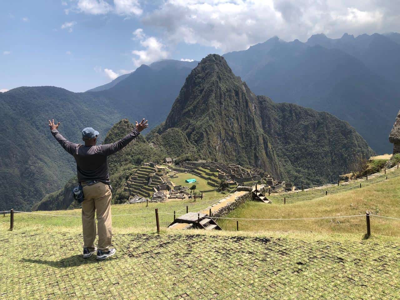 Person enjoying panoramic view of Machu Picchu and surrounding mountains.