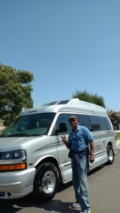Man standing next to a NomadicStan camper van on a sunny day.