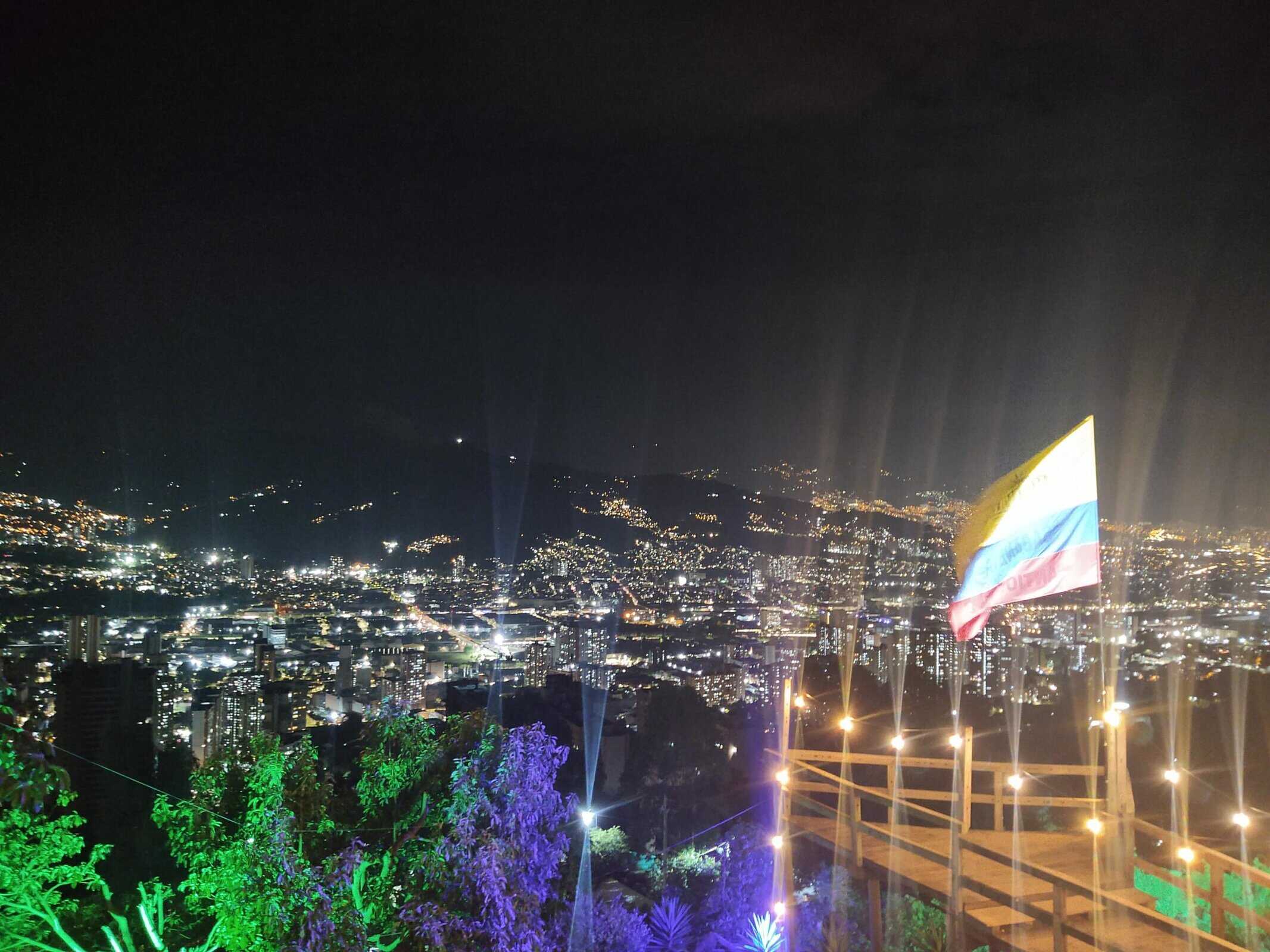 Vibrant cityscape at night with colorful lights and a flag, showcasing urban beauty and night life in Colombia. Medellin travel guide