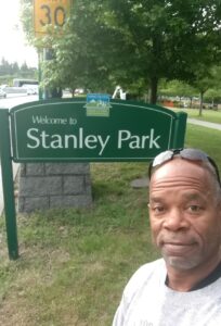 Man taking selfie in front of Stanley Park welcome sign.