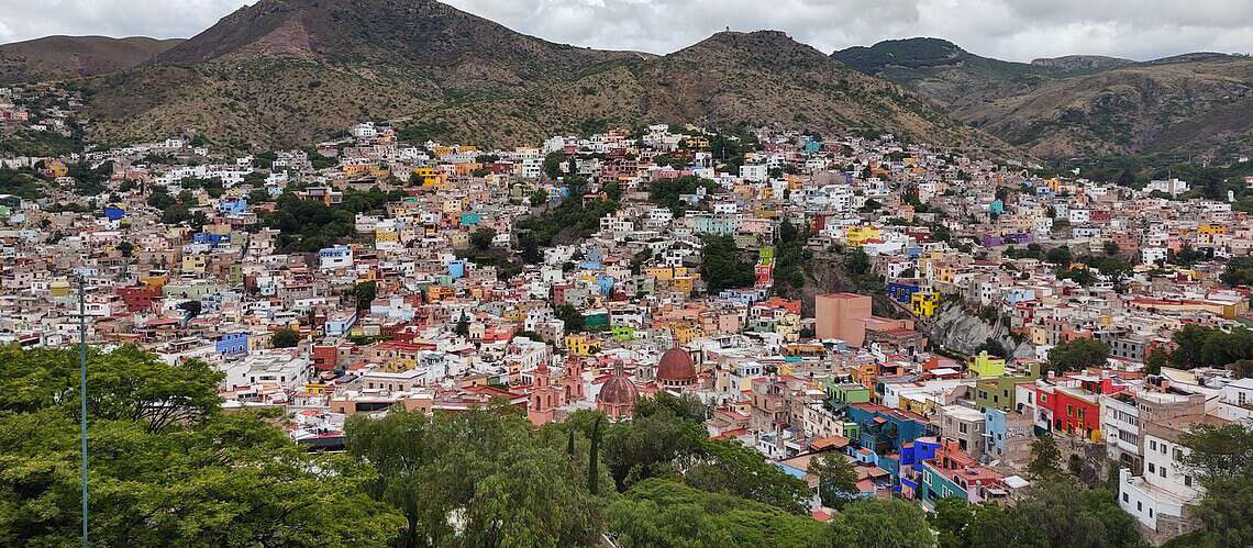 Vibrant hillside town with colorful buildings and mountains in the background.